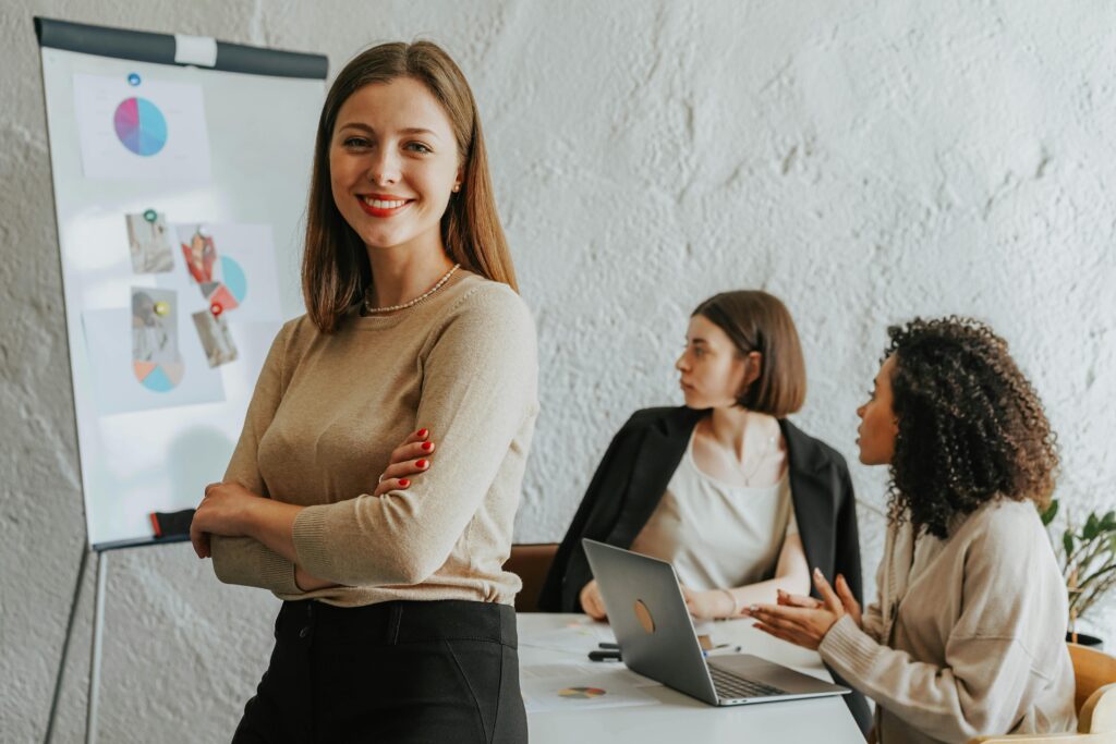 pexels photo 8145359 8145359 Confident woman smiling in a modern office setting with colleagues at work.